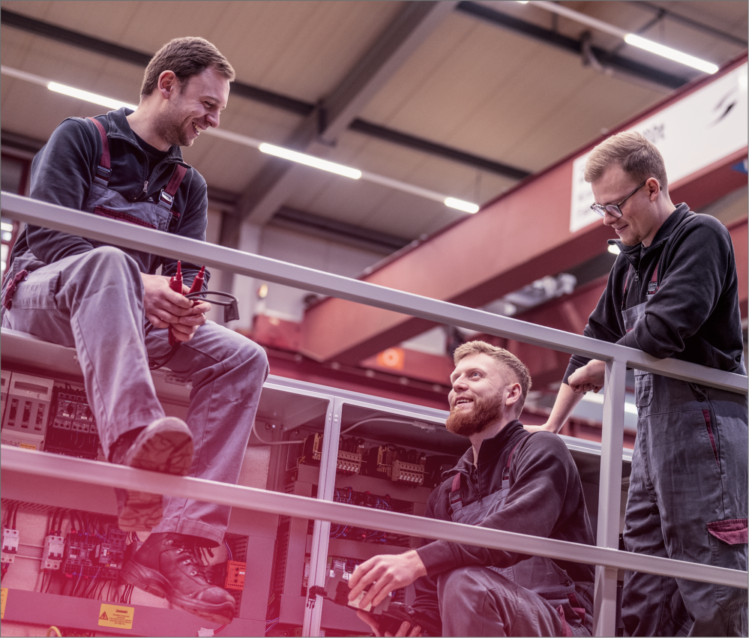 Drei Scheffer Mitarbeiter sitzen und stehen beinander. Alle tragen graue Latzhosen von Scheffer Krantechnik.